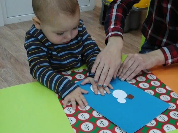 Педагог помогает малышу клеить ватный диск на картон
