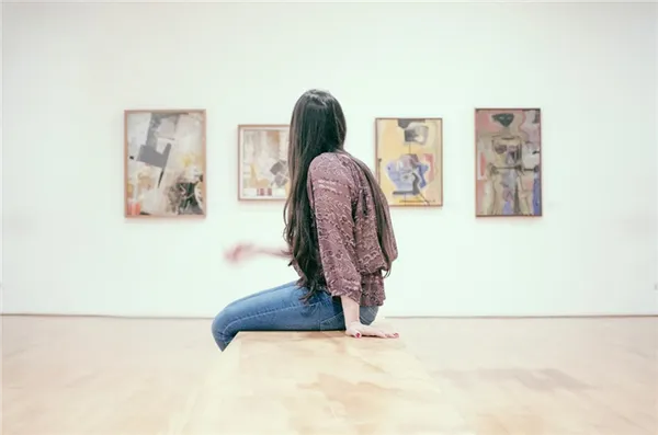 Девушка сидит на подиуме в картинной галерее