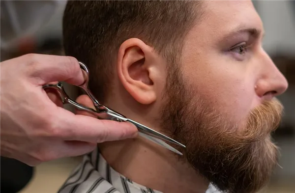 Мужчине подстригают бороду ножницами